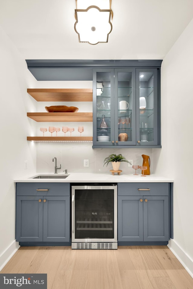 bar with sink, beverage cooler, light wood-type flooring, and decorative backsplash