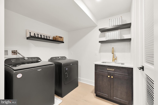 laundry room with cabinets, light hardwood / wood-style floors, washer and clothes dryer, and sink