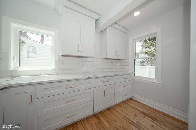 kitchen featuring white cabinets, decorative backsplash, light wood-type flooring, and light stone counters