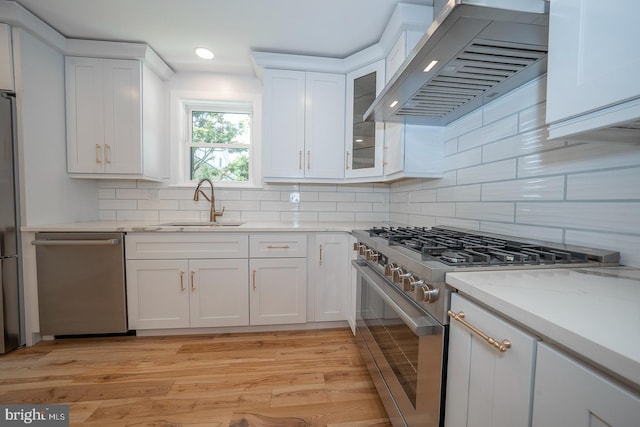 kitchen with white cabinets, stainless steel appliances, light hardwood / wood-style floors, and wall chimney range hood