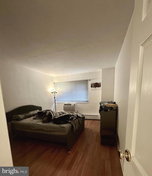 bedroom featuring a baseboard heating unit, a wall unit AC, and dark wood-type flooring