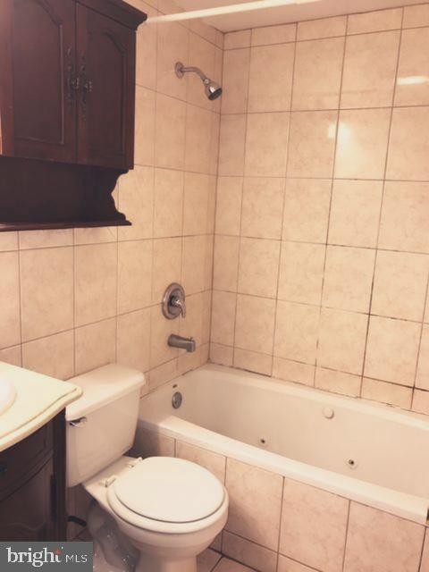 full bathroom featuring vanity, toilet, tiled shower / bath, and tile walls