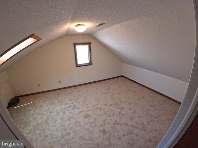 bonus room with a textured ceiling, vaulted ceiling with skylight, and carpet