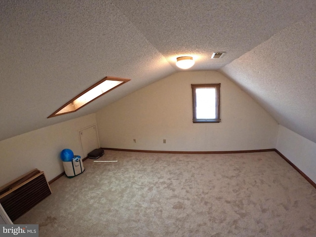 additional living space with a textured ceiling, carpet floors, and vaulted ceiling with skylight