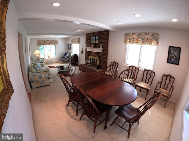 carpeted dining room with beam ceiling and a brick fireplace