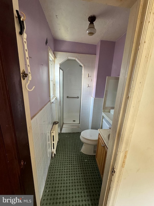 bathroom with walk in shower, vanity, tile walls, radiator heating unit, and toilet