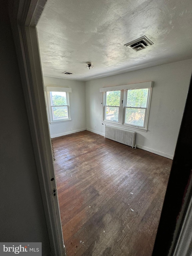 spare room with dark wood-type flooring, radiator heating unit, and a healthy amount of sunlight