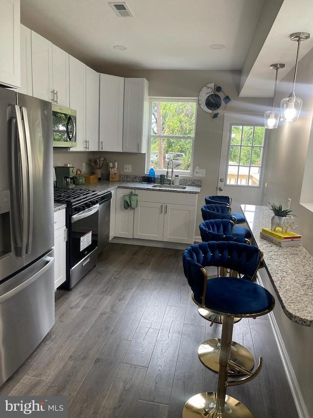 kitchen featuring pendant lighting, sink, appliances with stainless steel finishes, white cabinetry, and wood-type flooring