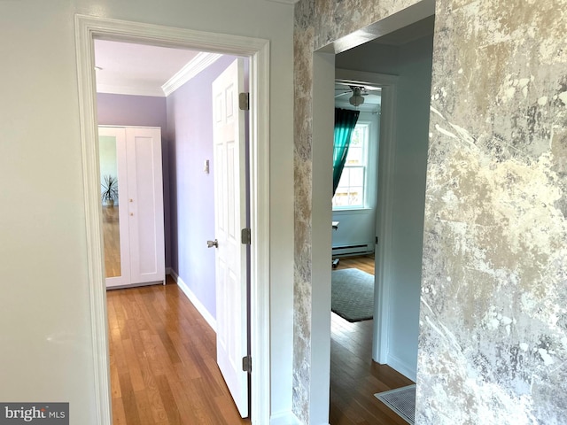 hallway with wood-type flooring, a baseboard heating unit, and crown molding