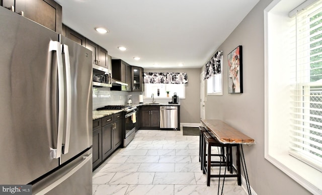 kitchen with appliances with stainless steel finishes, backsplash, a kitchen breakfast bar, light stone counters, and sink