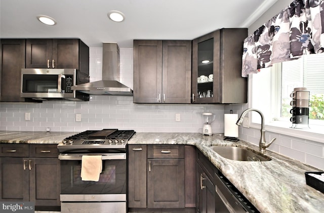 kitchen featuring backsplash, wall chimney range hood, sink, appliances with stainless steel finishes, and dark brown cabinets