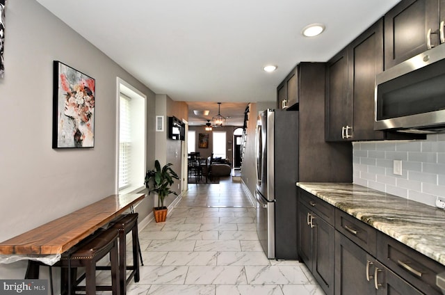 kitchen with appliances with stainless steel finishes, tasteful backsplash, light stone counters, dark brown cabinets, and a chandelier