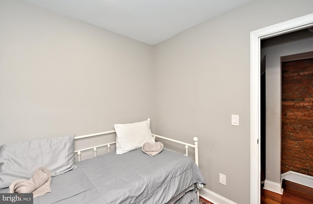 bedroom featuring hardwood / wood-style floors and brick wall