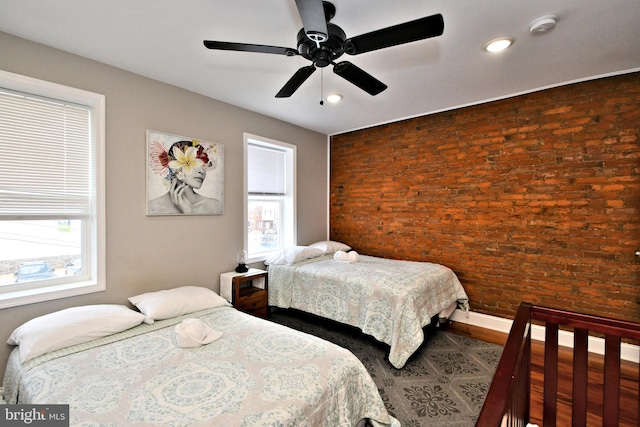 bedroom with multiple windows, ceiling fan, and brick wall