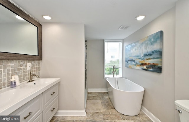 bathroom featuring vanity, backsplash, toilet, and a tub