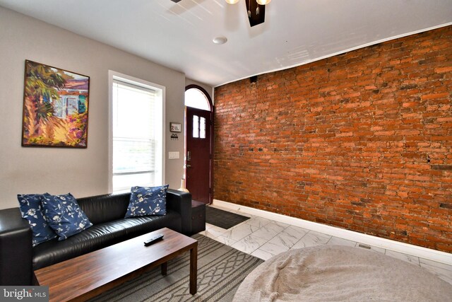 unfurnished living room with ceiling fan and brick wall