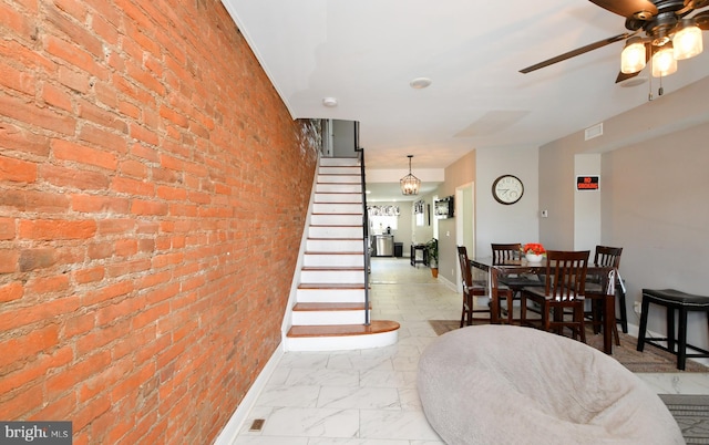 dining room featuring brick wall and ceiling fan with notable chandelier