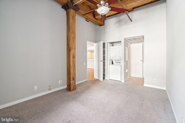 unfurnished bedroom with stacked washer / dryer, ceiling fan, light colored carpet, and a high ceiling