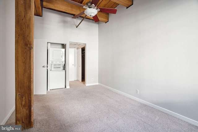 carpeted spare room with wood ceiling, ceiling fan, beamed ceiling, and stacked washing maching and dryer