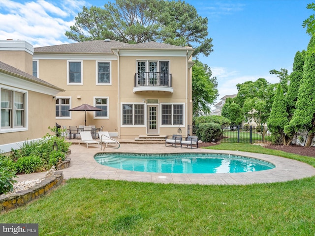 rear view of house featuring a balcony, a fenced in pool, a patio area, and a lawn