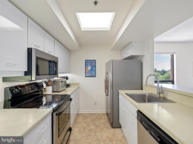 kitchen with a skylight, sink, stainless steel appliances, light tile patterned floors, and white cabinets