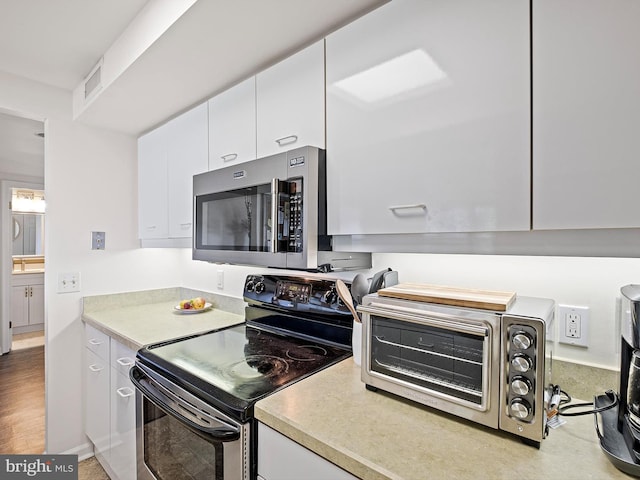 kitchen with white cabinetry, stainless steel appliances, and light hardwood / wood-style floors