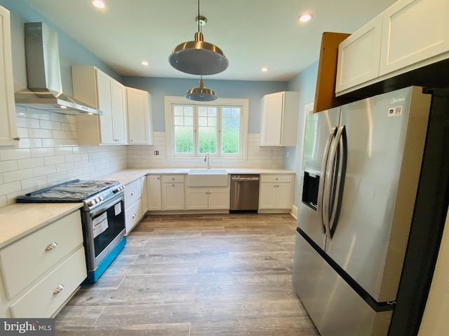 kitchen featuring pendant lighting, sink, stainless steel appliances, white cabinets, and wall chimney exhaust hood