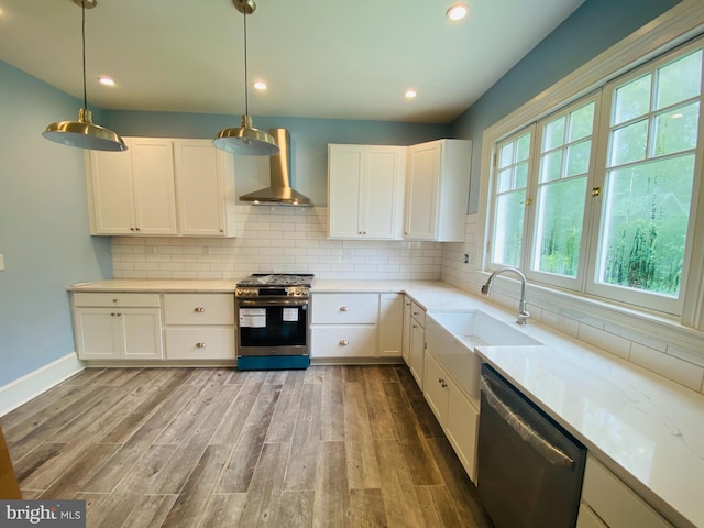 kitchen with wall chimney exhaust hood, sink, white cabinetry, appliances with stainless steel finishes, and pendant lighting