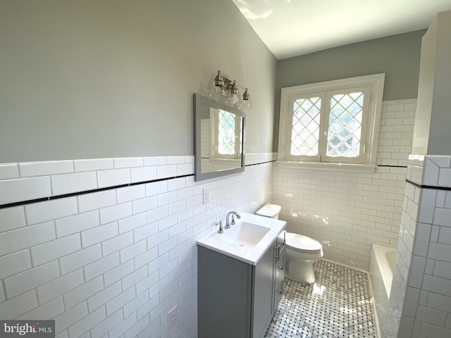 bathroom with tile walls, a bathtub, vanity, toilet, and tile patterned floors