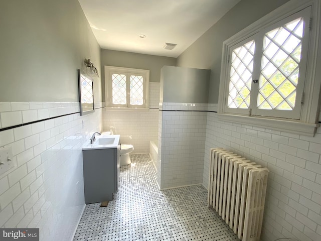 bathroom featuring vanity, toilet, radiator, and tile walls