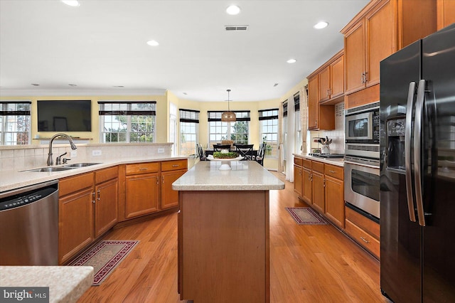 kitchen with sink, appliances with stainless steel finishes, a kitchen island, pendant lighting, and light hardwood / wood-style floors