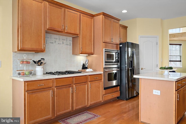 kitchen with decorative backsplash, appliances with stainless steel finishes, a kitchen island, and light wood-type flooring