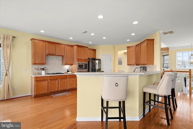 kitchen featuring a breakfast bar, appliances with stainless steel finishes, tasteful backsplash, kitchen peninsula, and light wood-type flooring