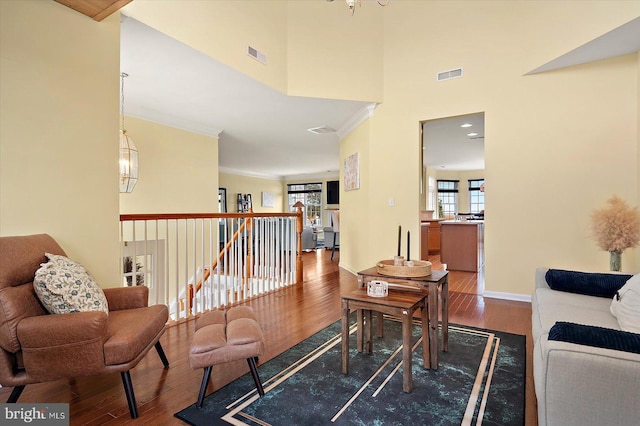 living room with hardwood / wood-style flooring, ornamental molding, an inviting chandelier, and a high ceiling