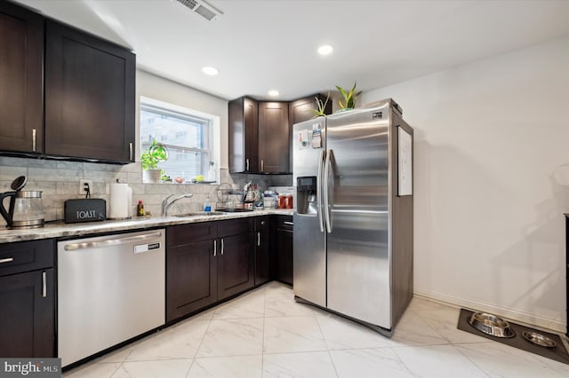 kitchen featuring light stone countertops, stainless steel appliances, decorative backsplash, sink, and dark brown cabinets