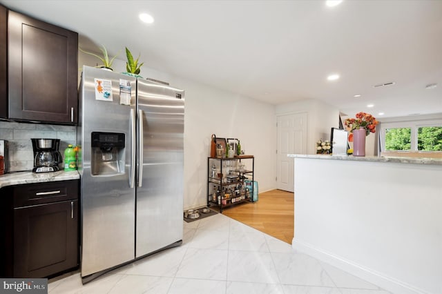 kitchen with decorative backsplash, light stone countertops, stainless steel fridge with ice dispenser, and dark brown cabinetry