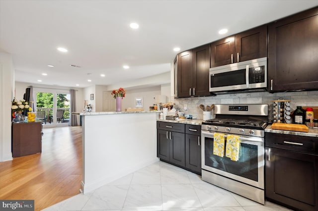 kitchen featuring kitchen peninsula, light stone countertops, decorative backsplash, and stainless steel appliances