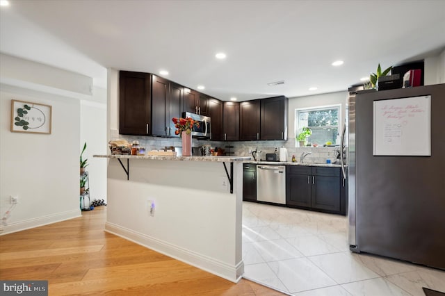 kitchen with a breakfast bar area, stainless steel appliances, backsplash, light stone counters, and dark brown cabinetry