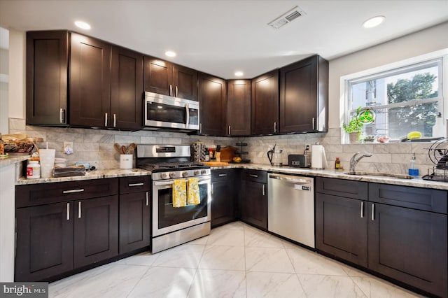 kitchen with light stone countertops, appliances with stainless steel finishes, backsplash, and sink