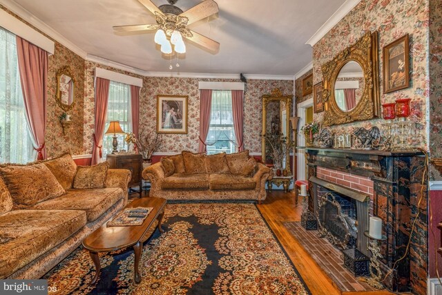 living room featuring a brick fireplace, hardwood / wood-style flooring, ceiling fan, ornamental molding, and plenty of natural light