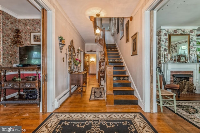 entrance foyer featuring crown molding, wood-type flooring, baseboard heating, and a brick fireplace