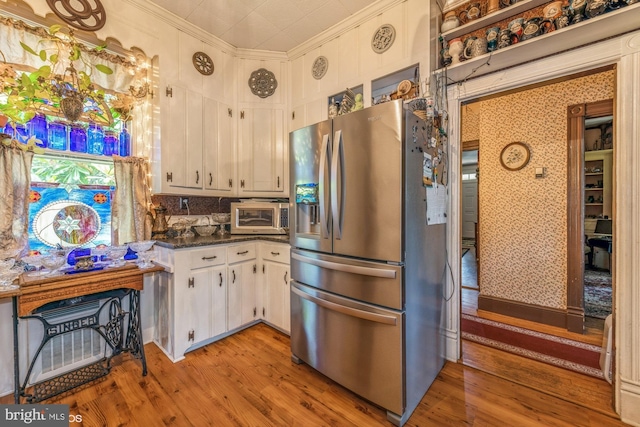 kitchen featuring dark stone counters, light wood-type flooring, ornamental molding, white cabinetry, and stainless steel appliances