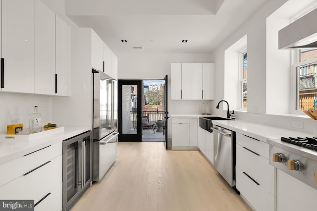 kitchen featuring plenty of natural light, white cabinetry, stainless steel appliances, and beverage cooler