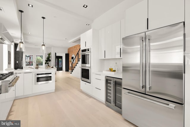 kitchen featuring pendant lighting, stainless steel appliances, white cabinetry, and light hardwood / wood-style floors