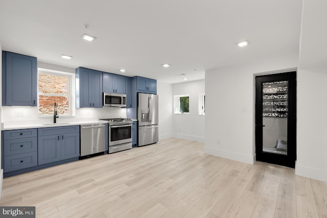 kitchen with appliances with stainless steel finishes, light hardwood / wood-style floors, blue cabinets, and sink