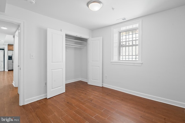 unfurnished bedroom with hardwood / wood-style floors, stainless steel fridge, and a closet