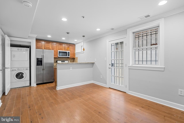 kitchen with kitchen peninsula, appliances with stainless steel finishes, decorative light fixtures, light hardwood / wood-style floors, and stacked washer / drying machine