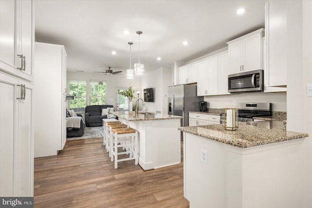 kitchen featuring stainless steel appliances, a kitchen breakfast bar, open floor plan, white cabinets, and a center island with sink