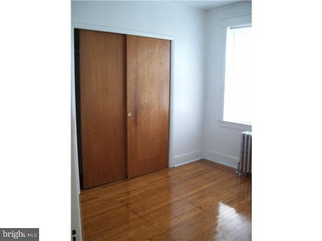 unfurnished bedroom with radiator, a closet, and hardwood / wood-style flooring