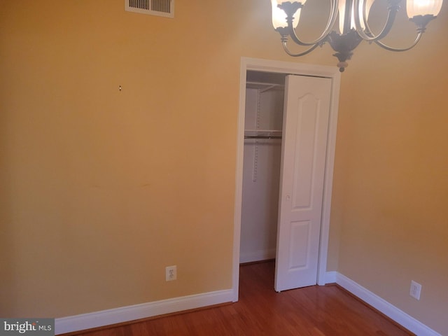 unfurnished bedroom featuring a closet, a chandelier, and hardwood / wood-style flooring